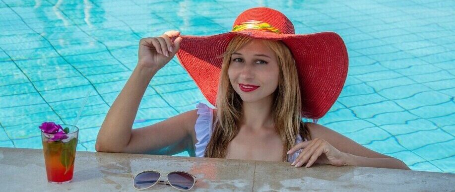 Woman smiling in a swimming pool at Riu Palace Paradise Island, adjusting her sombrero under sunny skies.